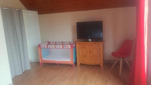 Zimmer mit einem TV auf einer Holzkommode mit einem Stuhl in der Unterkunft Au rayon de soleil in Trédias