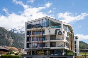 a large white building with mountains in the background at Lifesteil Aparthotel in Umhausen