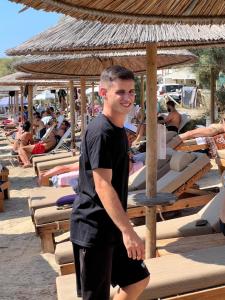 a man standing on a beach with people on lounge chairs at Manios Suites in Agia Anna Naxos