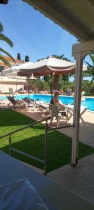 a man sitting in a chair under an umbrella next to a pool at Helena Inn in Svoronata