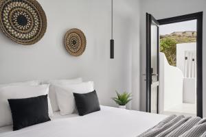 a white bedroom with a white bed with black pillows at The Thermia Suites in Kithnos