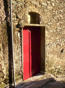 una porta rossa sul lato di un edificio in pietra di OLMETA DI TUDA - T3 a Olmeta-di-Tuda