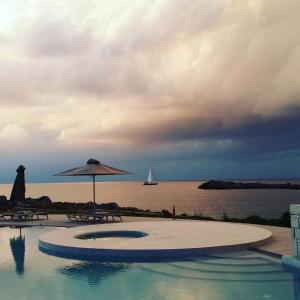 a swimming pool with an umbrella and a boat in the water at Kavos Hotel & Suites in Stavros