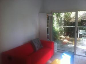 un sofá rojo en la sala de estar con una puerta corredera de cristal en Ardèche, studio indépendant dans jardin, en Chomérac