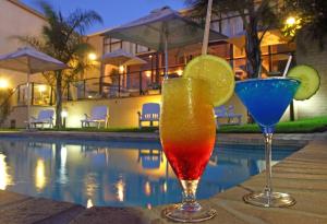 two cocktails are sitting next to a swimming pool at Hotel Portao Diaz in Mossel Bay