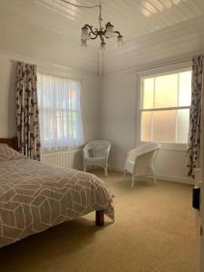 a bedroom with a bed and two chairs and two windows at Vine Cottage - Sandgate in Sandgate