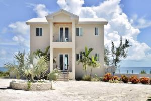 a white house with the ocean in the background at Cupid's Way is a High-end New Home with Large PRIVATE Pool Snorkeling Cliff Jumping and Water Sports Equipment in Governorʼs Harbour