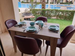 - une table en bois avec des chaises et des assiettes dans l'établissement Mangroovy - Delicate 1BR Ground floor by the Pool, à Hurghada