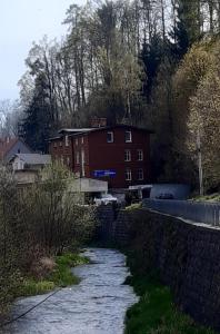a river in front of a red building and a house at Apartament nad rzeką in Głuszyca