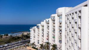 a white building with the ocean in the background at Tamara Ashkelon Hotel in Ashkelon