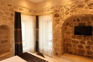Mardin Bey Konağı Hotel في ماردين: غرفة نوم بحائط حجري مع نافذة وتلفزيون