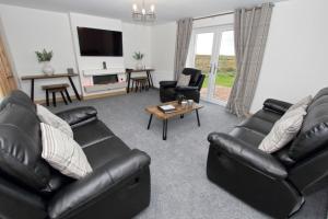 a living room with black leather furniture and a tv at Sea Breeze in Clachan