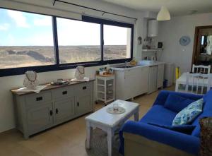 a living room with a blue couch and a kitchen with large windows at Casa Maria Cotillo Mar in El Cotillo