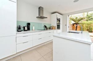 a kitchen with white cabinets and a sink at Family Home near Clapham Common by UnderTheDoormat in London