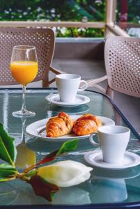 a glass table with two plates of croissants and an orange juice at NikoleTakis Apartments in Paralia Panteleimonos
