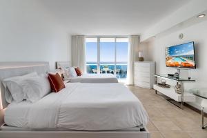 a white bedroom with two beds and a television at Ocean View Balcony steps from Restaurants, Peacock Park & Marina in Miami