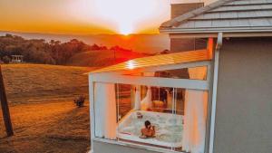 a person sitting in a tub in a window with the sunset at Casa Paraíso do Sol - Rancho Queimado - SC in Rancho Queimado