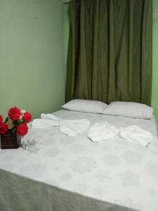 ムクジェーにあるPousada Recanto da Villaの白いシーツと赤い花が飾られたベッド