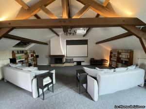 una stanza con due divani e uno schermo in un edificio di Séjour de charme à Mareau-aux-Bois : parc, home cinéma, billard, tennis et télétravail en fibre ultra-rapide - FR-1-590-279 a Mareau-aux-Bois