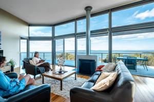 two people sitting in a living room with large windows at Halcyon ~ Immerse yourself in the sky and sea in Coles Bay