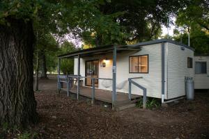 a small white tiny house with a porch next to a tree at Tawonga Tourist Park in Tawonga