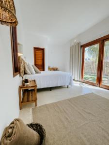 a white bedroom with a bed and a large window at Vila Caiada Guest House in Luis Correia