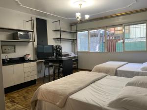 a bedroom with two beds and a desk with a television at Pousada Hostel Dodora in Bento Gonçalves