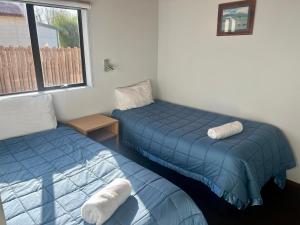 two beds in a room with blue sheets and a window at Pinewood Motels in Fairlie