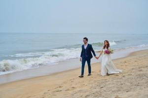 een bruid en bruidegom die op het strand lopen bij Maliekal Heritance Cherai Beach Cochin in Cherai Beach