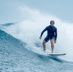 Un uomo che cavalca un'onda su una tavola da surf nell'oceano di Holiday Home Himmafushi a Himmafushi