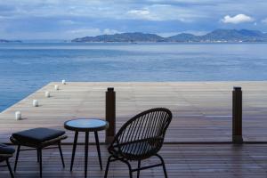 a wooden pier with chairs and a table and the water at SETO CLAS AJI THE SEASIDE HILLS RESORT in Aji