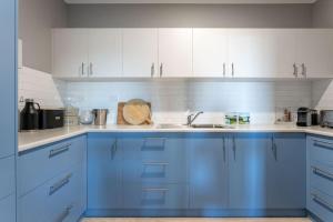 a blue kitchen with white cabinets and a sink at Belvoir - Denmark in Denmark
