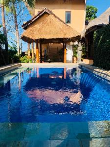 a large swimming pool with a straw hut next to a house at Giri's Villa Jimbaran in Ungasan
