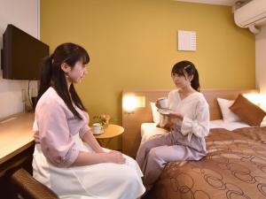 Dos mujeres sentadas en una cama en una habitación de hotel en Yokohama Heiwa Plaza Hotel, en Yokohama