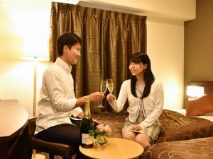 Ein Mann und eine Frau sitzen auf einem Bett mit Weingläsern in der Unterkunft Yokohama Heiwa Plaza Hotel in Yokohama