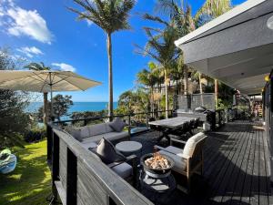 a deck with a couch and tables and an umbrella at Private Water Front House in Whangaparaoa