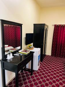 a hotel room with a desk and a refrigerator and red curtains at DANA HOTEL-Clock Tower Sharjah in Sharjah