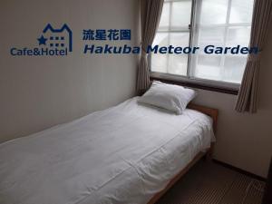 a small bedroom with a bed with white sheets and a window at Meteor Garden in Hakuba