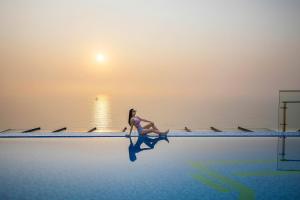 a woman sitting on the edge of a swimming pool at Maximilan Danang Beach Hotel in Da Nang