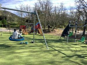 Um homem está sentado num baloiço num parque infantil. em Duplex (5pers) dans village vacances en Ardèche em Grospierres