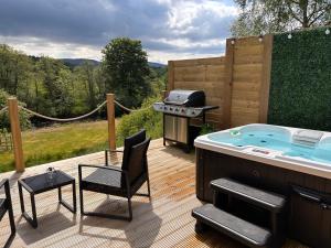 a hot tub on a deck with a grill and chairs at River Huts, Highland River Retreat with Hot Tub in Inverness