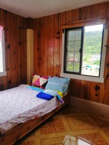een slaapkamer met houten wanden en een bed met een raam bij Inn Maugay Bed and Bath in Sagada
