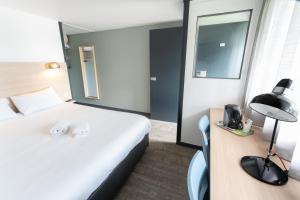 ラ・ロシェルにあるHotel Inn Design La Rochelleのベッド、ランプ付きのデスクが備わるホテルルームです。