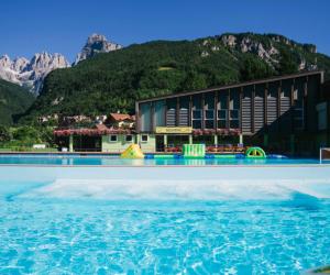 a swimming pool in front of a building with mountains at APPARTAMENTO LUAN in Andalo