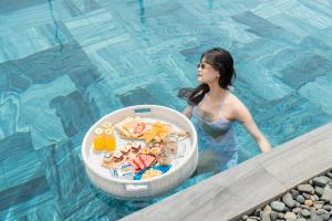 une femme dans une piscine avec un bol de nourriture dans l'établissement Seahorse Tropical Da Nang Hotel by Haviland, à Đà Nẵng