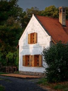 Casa blanca con ventanas de madera en un lateral. en Présház szállás a Szent György-hegyen, en Kisapáti