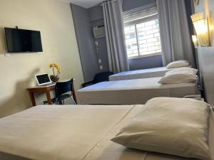 a hotel room with three beds and a laptop on a desk at Riviera Hotel in Brasília