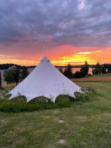 a white tent in a field with a sunset in the background at Amberhouse Glempings in Piejūti