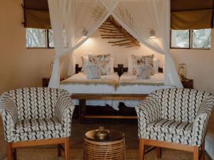 a bedroom with a white bed with two chairs at Nyala Safari Lodge in Hoedspruit