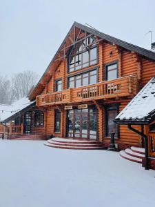 une grande maison en bois avec de la neige au sol dans l'établissement Батярський Двір, à Pasiky-Zubryts'ki